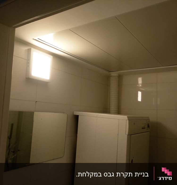 מכונת כביסה בחדר עם קירות גבס ותאורה עליונה